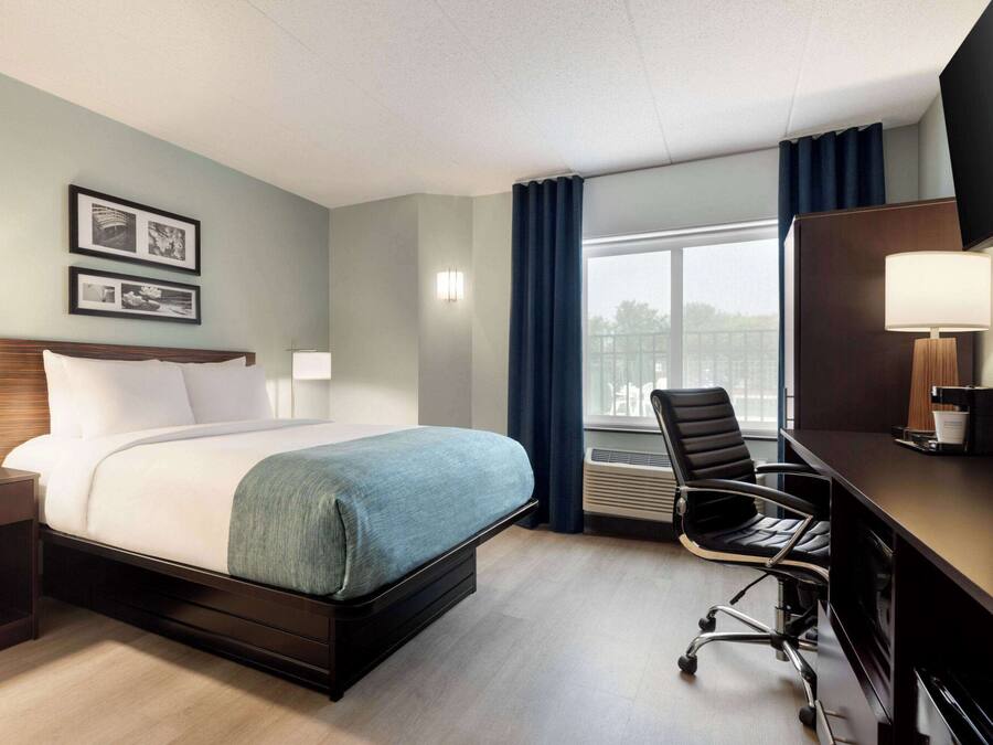Habitación de hotel con cama, mesitas de noche, escritorio, silla y un amplio ventanal con cortinas.
