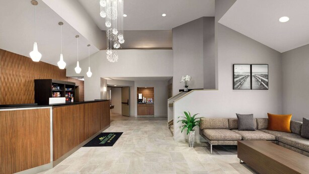 A modern lobby with a reception desk, a seating area with a sofa and a plant, and a staircase leading to an upper level. - Wingate by Wyndham Salisbury MD Airport North (Salisbury)