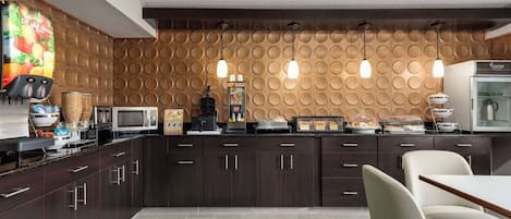 Una cocina moderna con armarios de madera oscura, microondas, cafetera y una barra de desayuno con vitrina de vidrio.