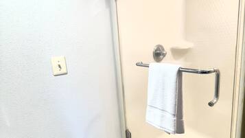 Ducha a pie con puerta de vidrio, un perchero y un interruptor de luz en la pared.