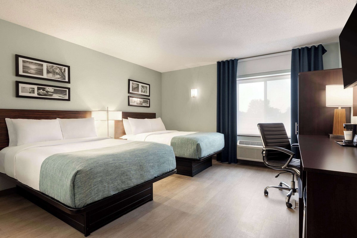 Habitación de hotel con dos camas, un escritorio, una silla y un ventanal con cortinas.