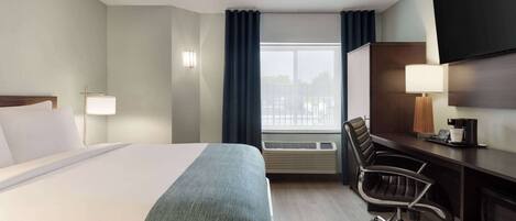 A hotel room with a bed, desk, chair, and a large TV on the wall.