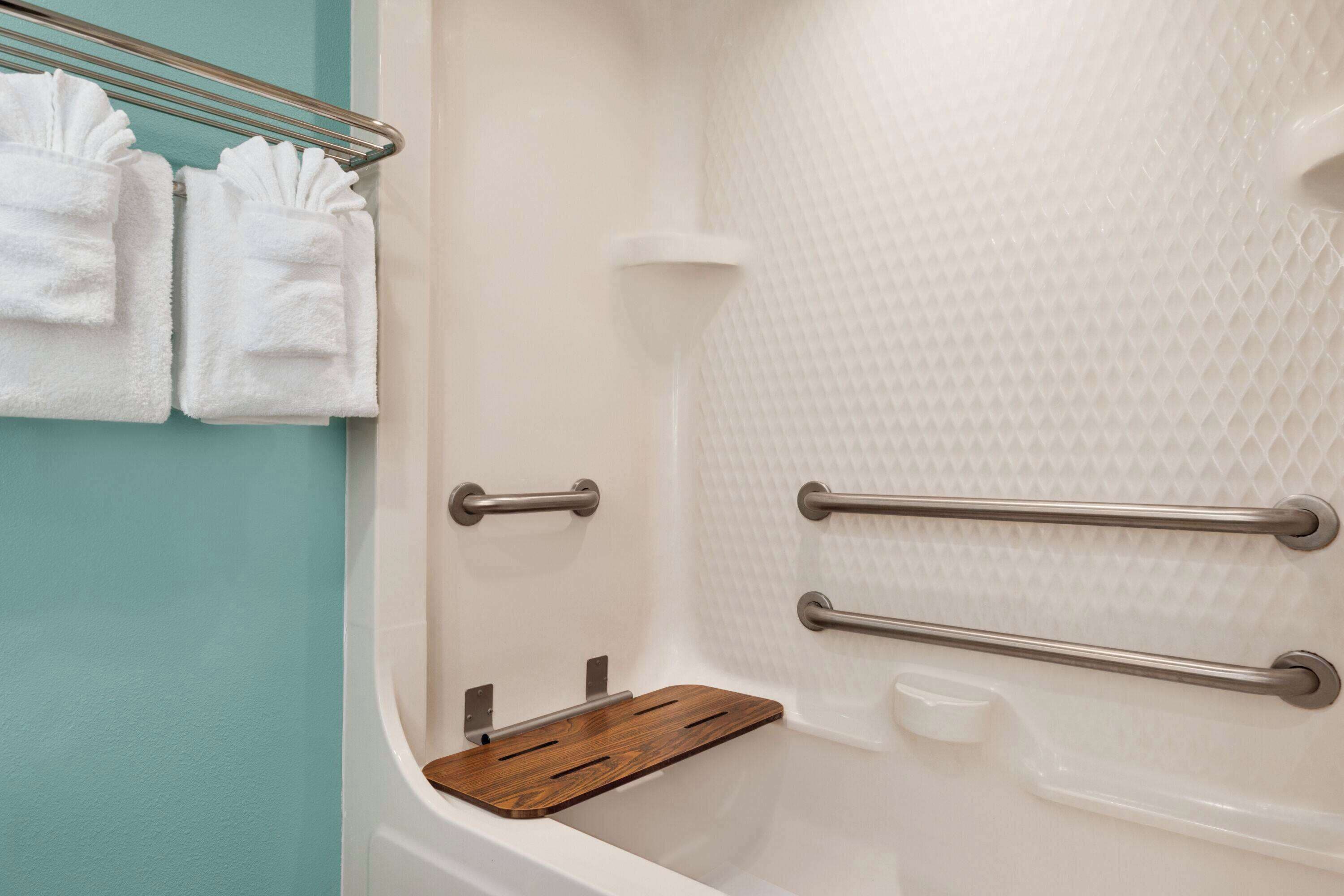 A bathroom with a white bathtub, a wooden shelf, and two towels hanging on a metal rack.