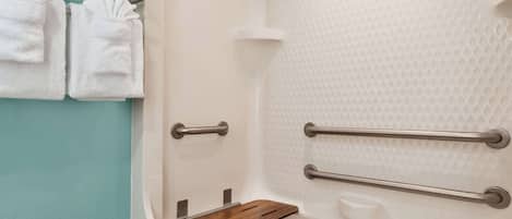 A bathroom with a white bathtub, a wooden shelf, and two towels hanging on a metal rack.