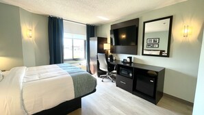 A hotel room with a bed, desk, chair, and a large TV.