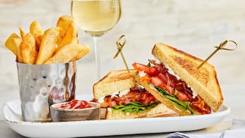 Un plato con un sándwich a la parrilla, una copa de vino blanco y un recipiente de papas fritas.