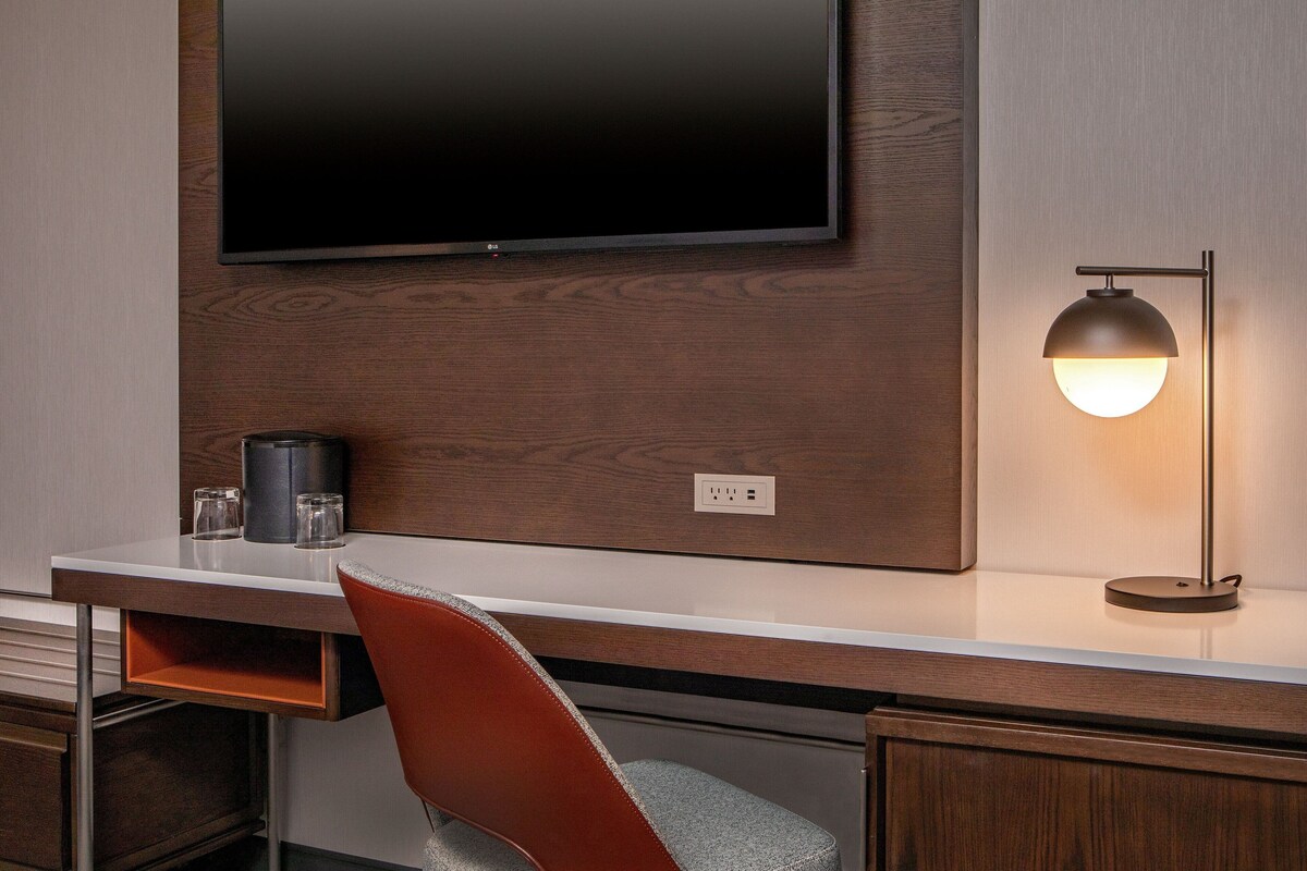 Een moderne hotelkamer met een flatscreen televisie aan de muur, een bureau met een lamp en een stoel.