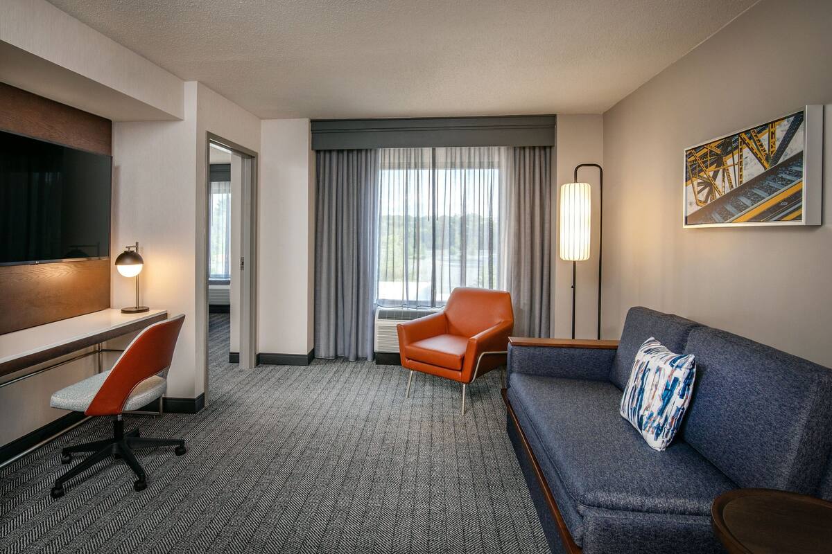 A hotel room with a desk, office chair, sofa, and a large window with curtains.