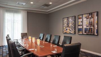 A conference room with a long table, black chairs, and two framed artworks on the wall.