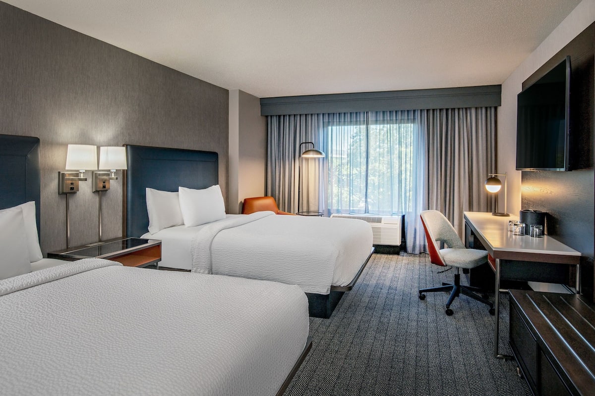 A hotel room with two beds, a desk, a chair, a TV, and a window with curtains.