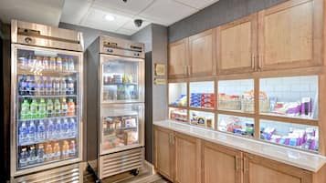 Una kitchenette con dos dispensadores de bebidas, un expositor de pan y una variedad de productos envasados.