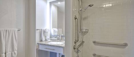 A bathroom with a shower, grab bars, a sink, and a towel rack.