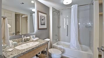 A modern bathroom with a granite countertop sink, a toilet, a bathtub, and a glass-enclosed shower.