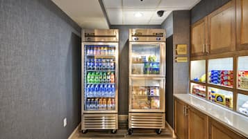 A kitchenette with two stainless steel refrigerators stocked with beverages and a freezer, and a counter with packaged snacks.