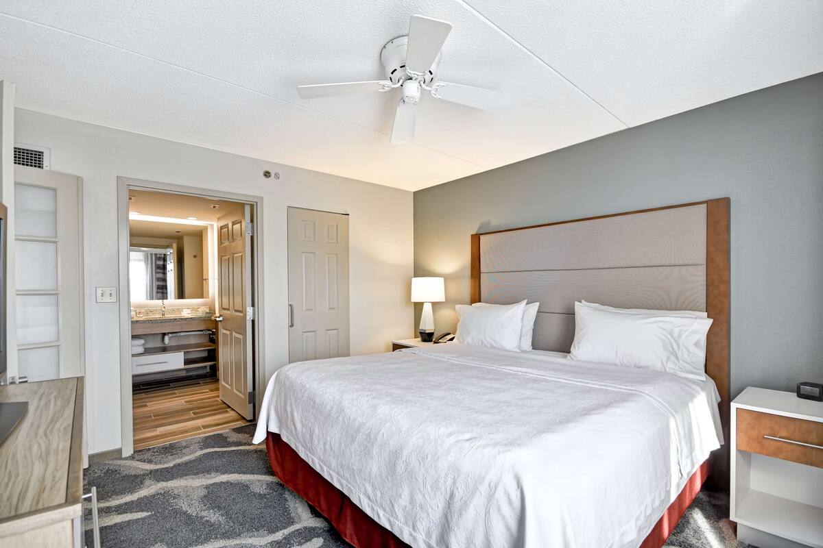 A hotel room with a bed, bedside table, lamp, and a ceiling fan.