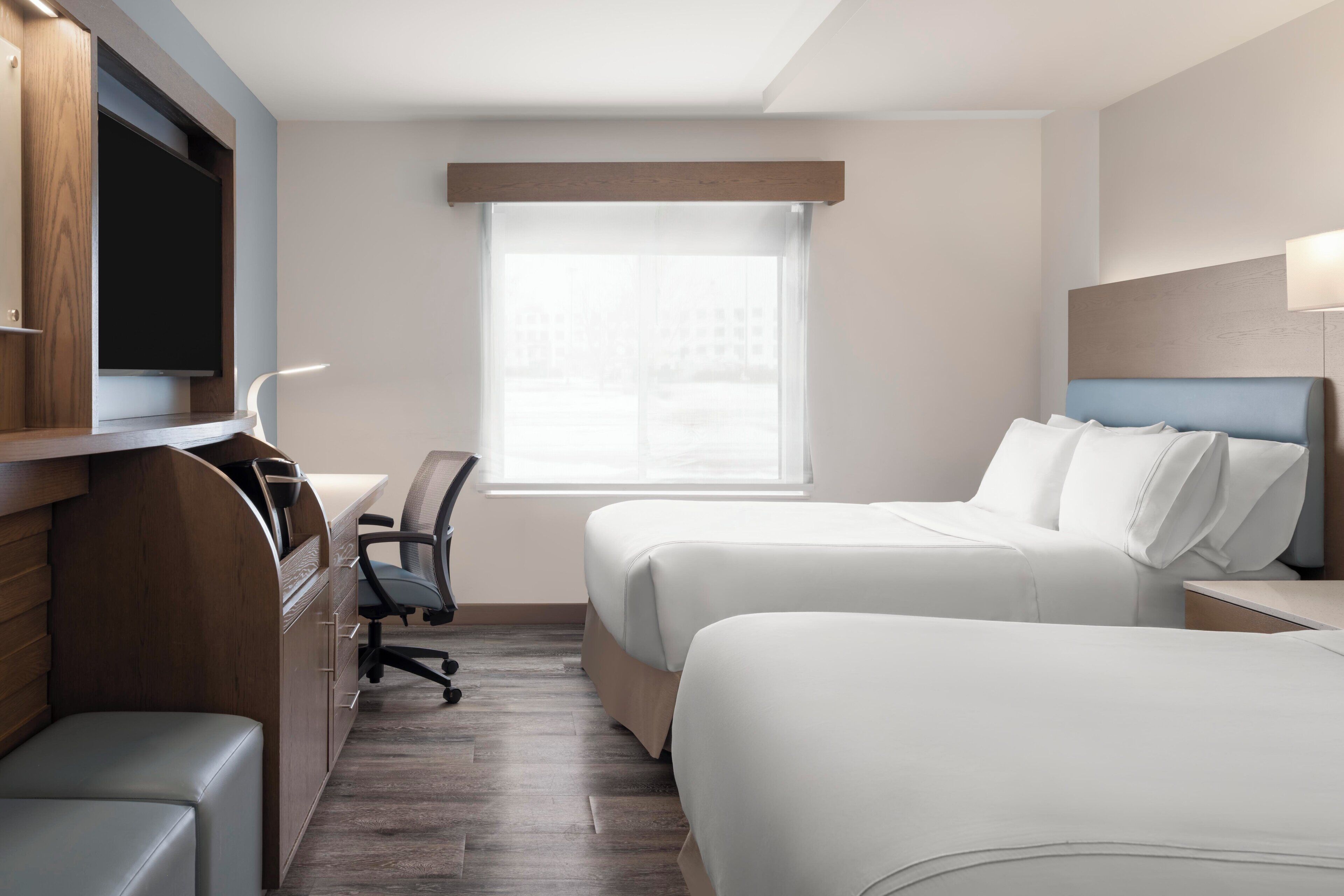 A hotel room with two beds, a desk, a chair, a TV, and a window.