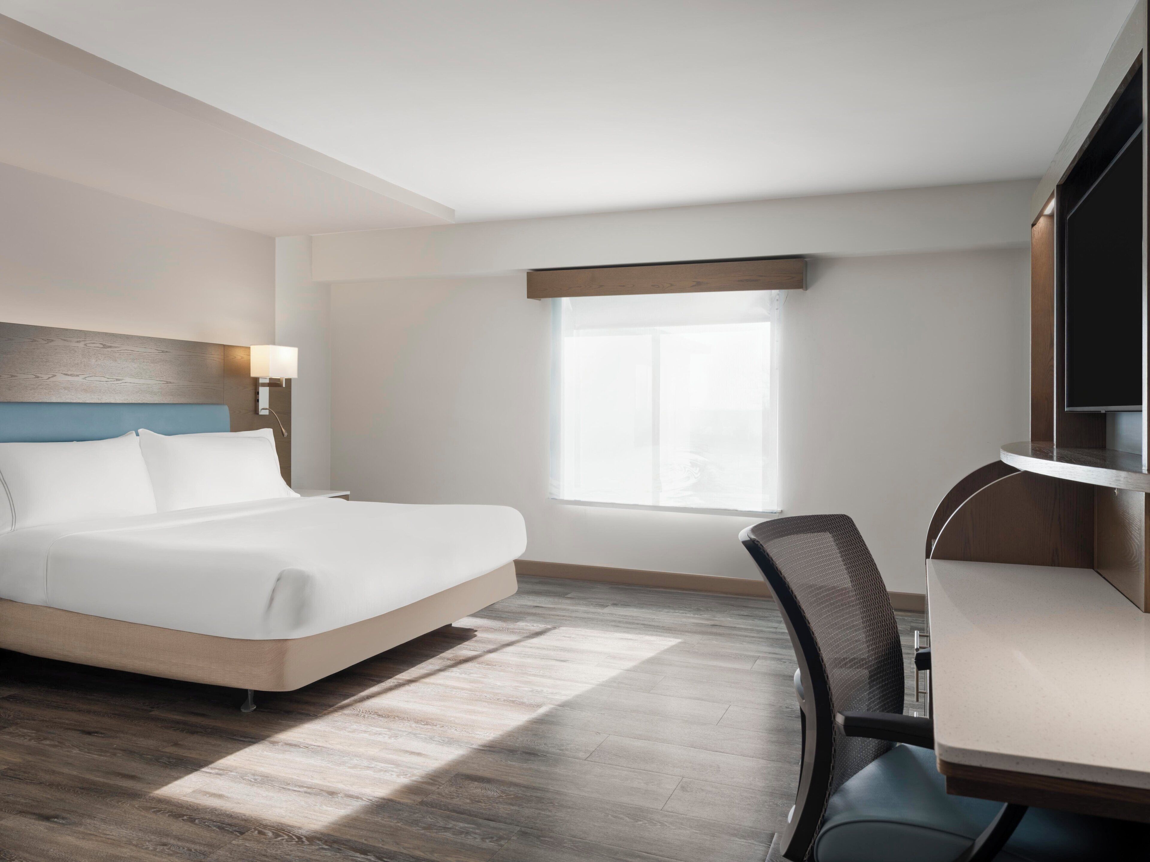 A hotel room with a bed, desk, chair, and a window.