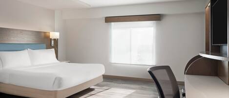 A hotel room with a bed, desk, chair, and a window.
