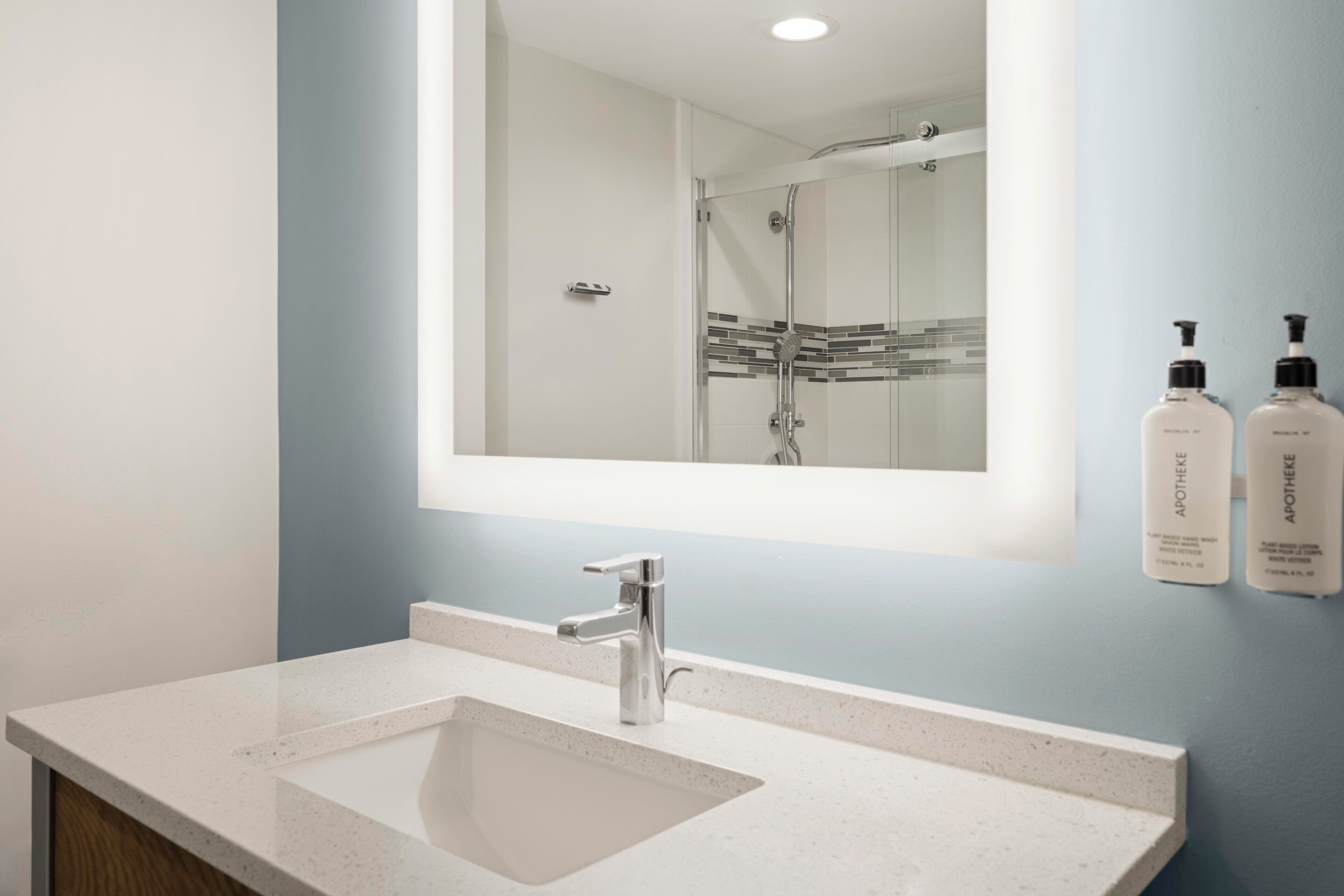 A bathroom with a large mirror, a sink, and two bottles of toiletries on the wall.