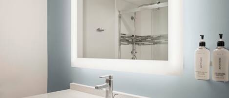 A bathroom with a large mirror, a sink, and two bottles of toiletries on the wall.