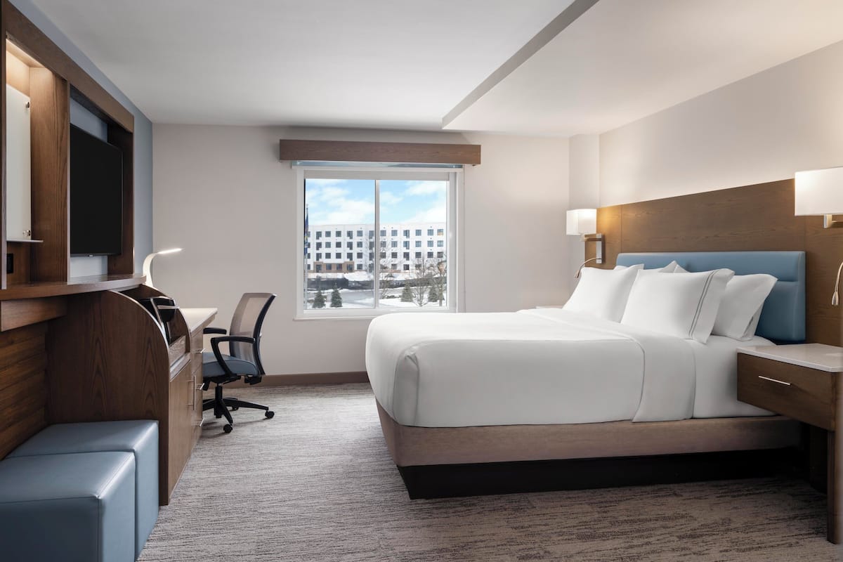 A hotel room with a bed, desk, chair, and a television.