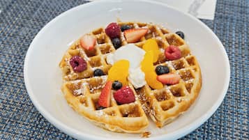 A plate of waffles with fruit and whipped cream.