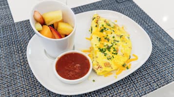 Un plato con una tortilla, un bol de fruta y un recipiente pequeño con salsa.
