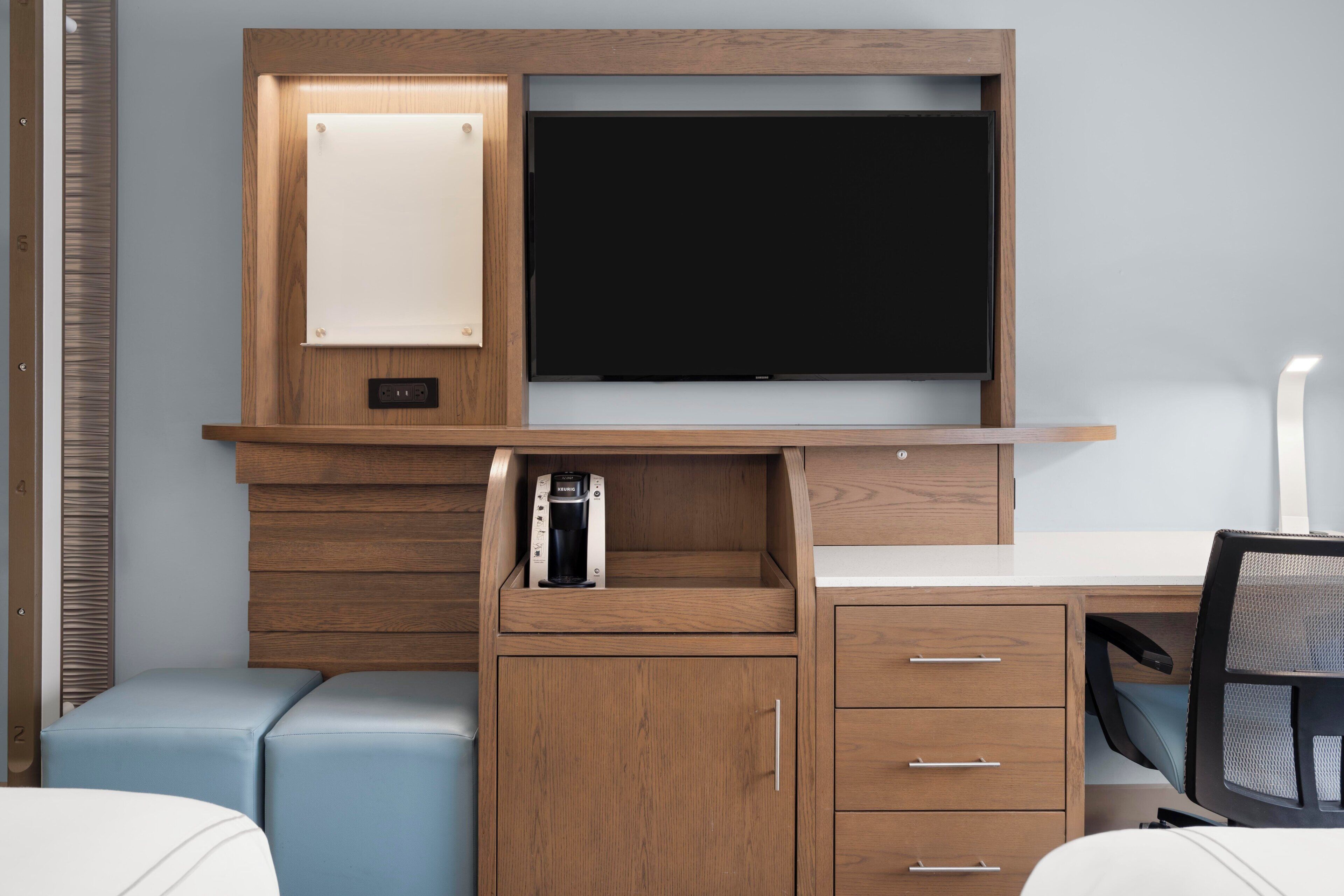 Ein modernes Zimmer mit Schreibtisch aus Holz, einem Flachbildfernseher, einer Kaffeemaschine und einem Stuhl.