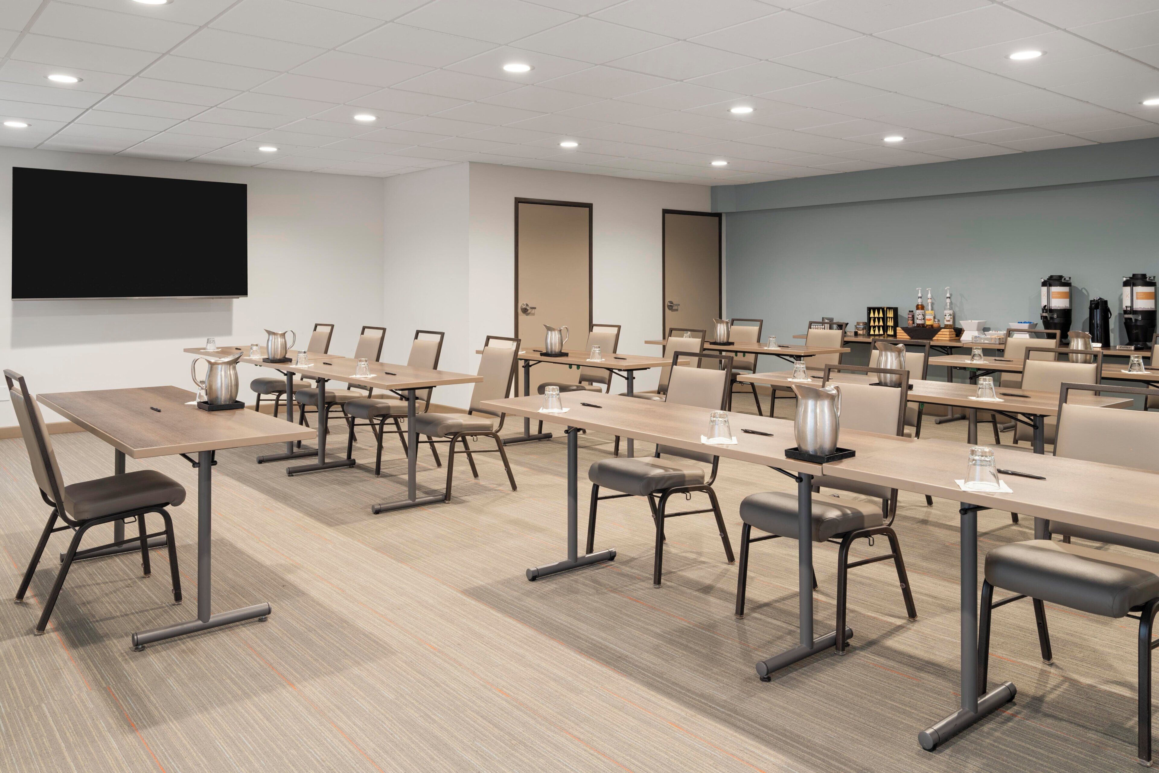 A conference room with multiple tables, chairs, a large screen, and a coffee station.