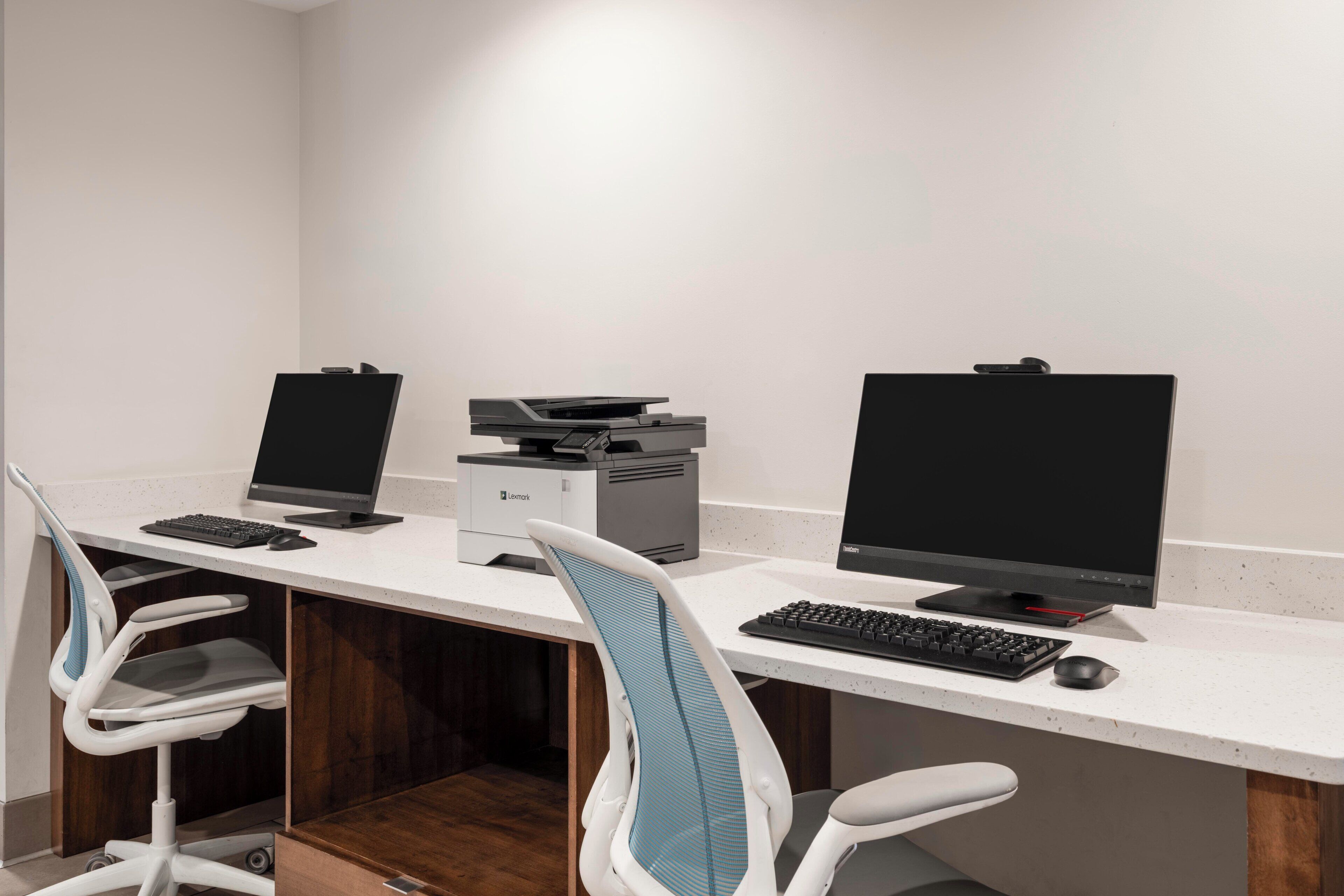 Un bureau moderne équipé de deux postes de travail, chacun comprenant un écran d’ordinateur, un clavier et une souris. On y trouve également deux chaises de bureau, dont une avec un dossier en tissu résille bleu.