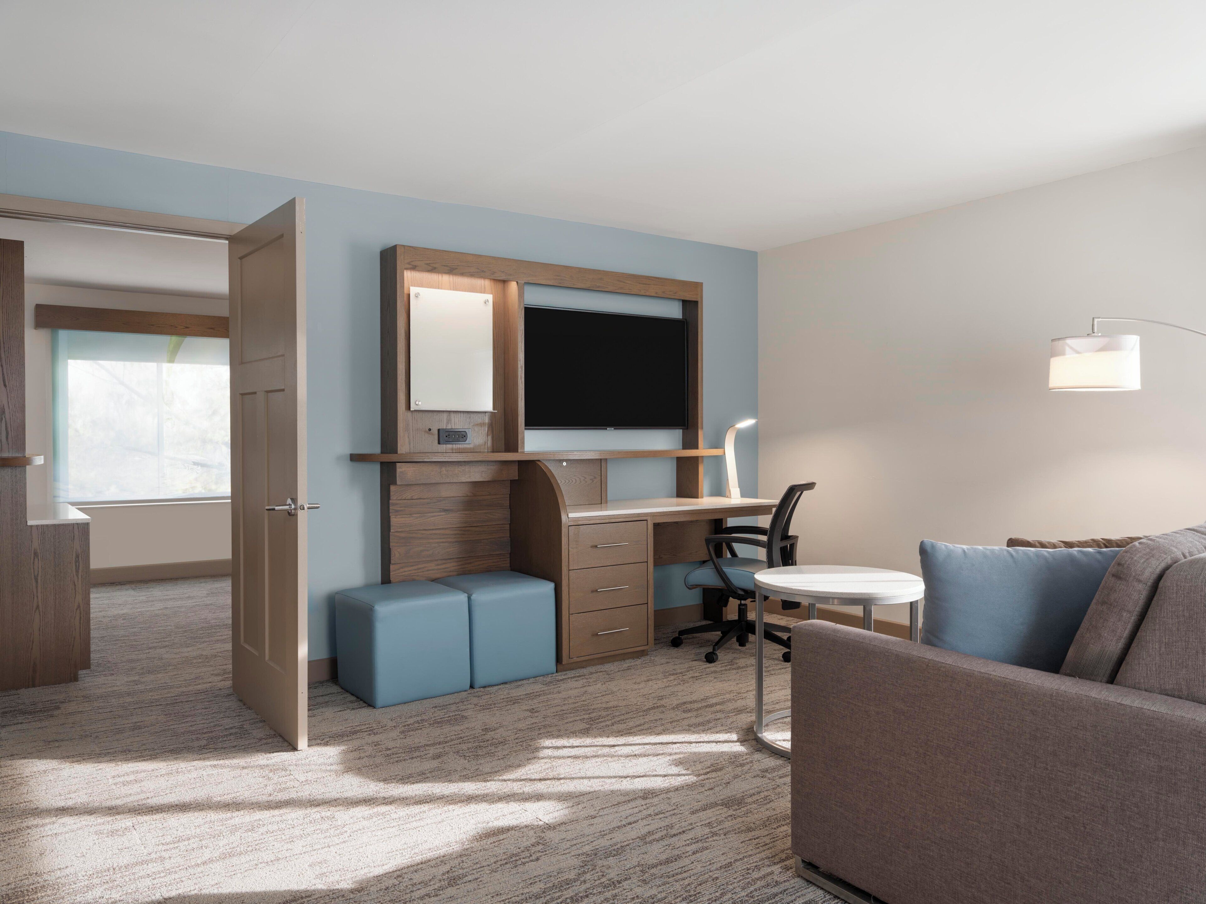 A hotel room with a desk, chair, sofa, and a television.