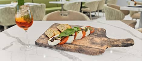 A dining table with a wooden board holding a dish of tomato and mozzarella, accompanied by a glass of red wine.