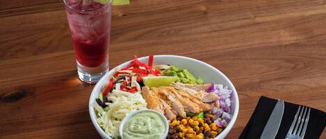 Eine Mahlzeit mit verschiedenen Speisen, darunter ein Salat, eine Schüssel Guacamole und ein Glas gekühltes Getränk mit einer Limettenscheibe.