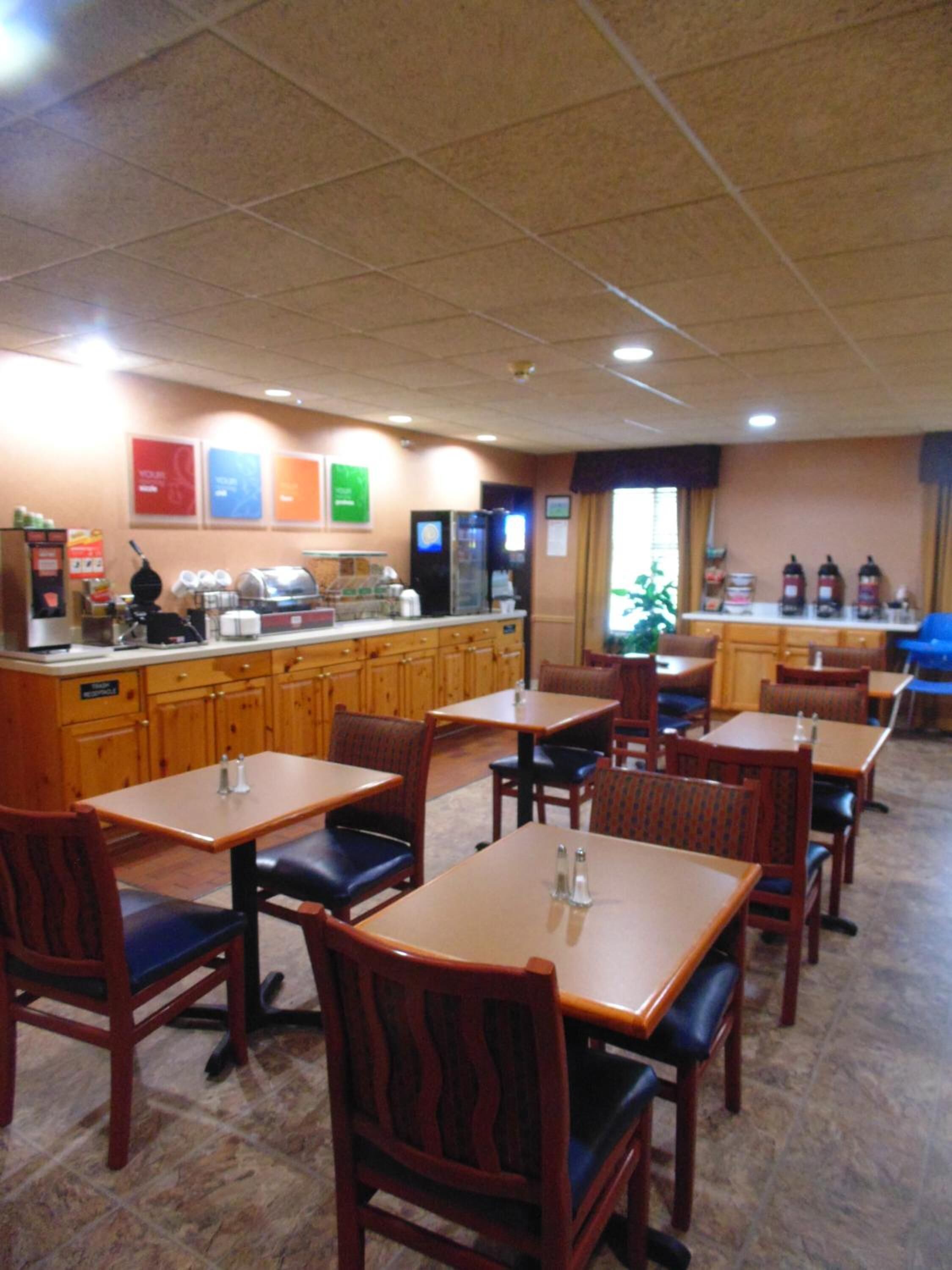 Ein Restaurant mit Holztischen und -stühlen, einer Theke mit einer Kaffeemaschine und einem Kühlschrank.