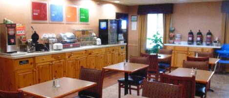 A restaurant with wooden tables and chairs, a counter with a coffee machine, and a refrigerator.