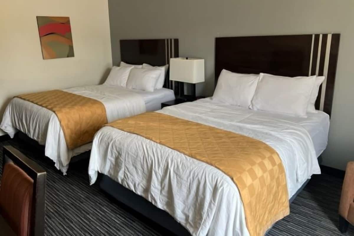 A hotel room with two beds, each with a headboard and a bedside lamp.