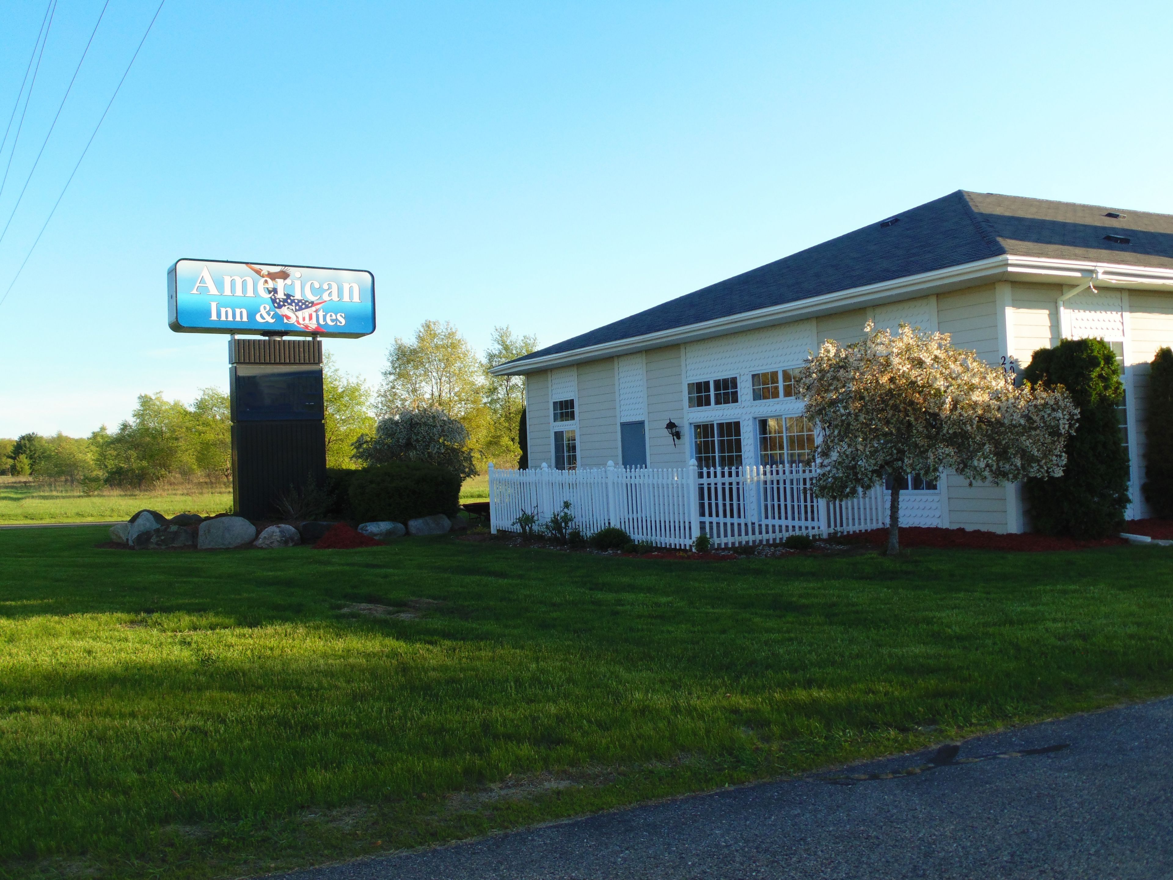 Un hôtel-motel de type américain, avec une clôture en bois peinte en blanc, une pelouse bien entretenue et un ciel dégagé.