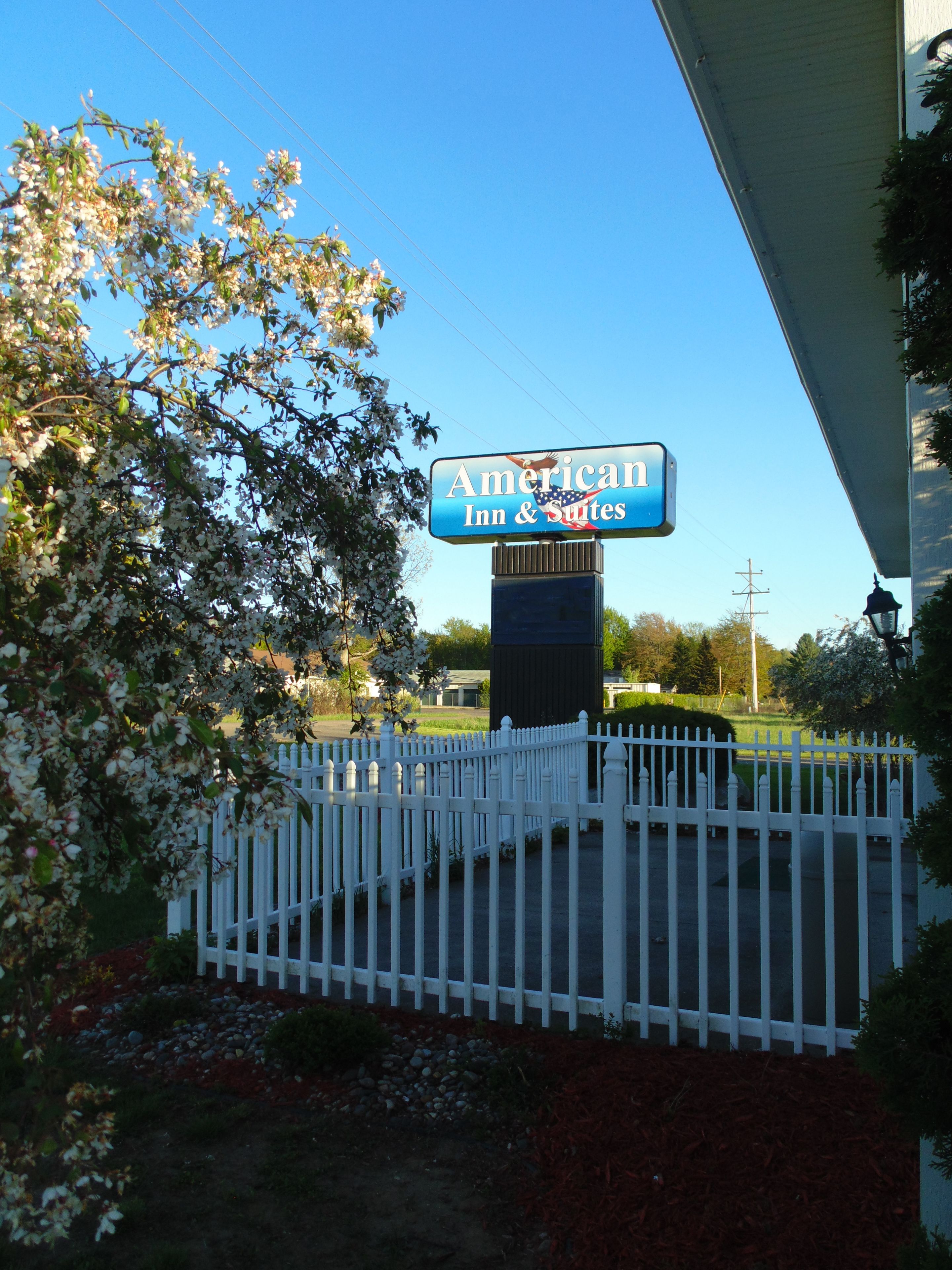 Un letrero para American Inn & Suites con una cerca blanca de piquetes al frente.