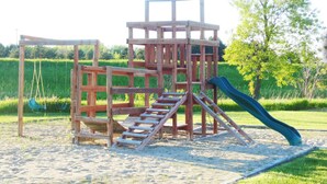 A wooden play structure with a slide and swings on a sandy beach. - American Inn and Suites Houghton Lake (Houghton Lake)