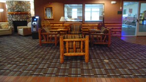 A lobby with a checkered floor, wooden furniture, a stone wall, and a fireplace. - American Inn and Suites Houghton Lake (Houghton Lake)
