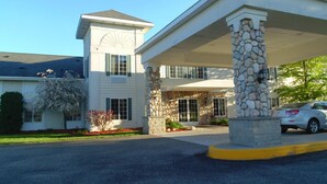 A two-story building with a stone facade and a covered entrance area. - American Inn and Suites Houghton Lake (Houghton Lake)