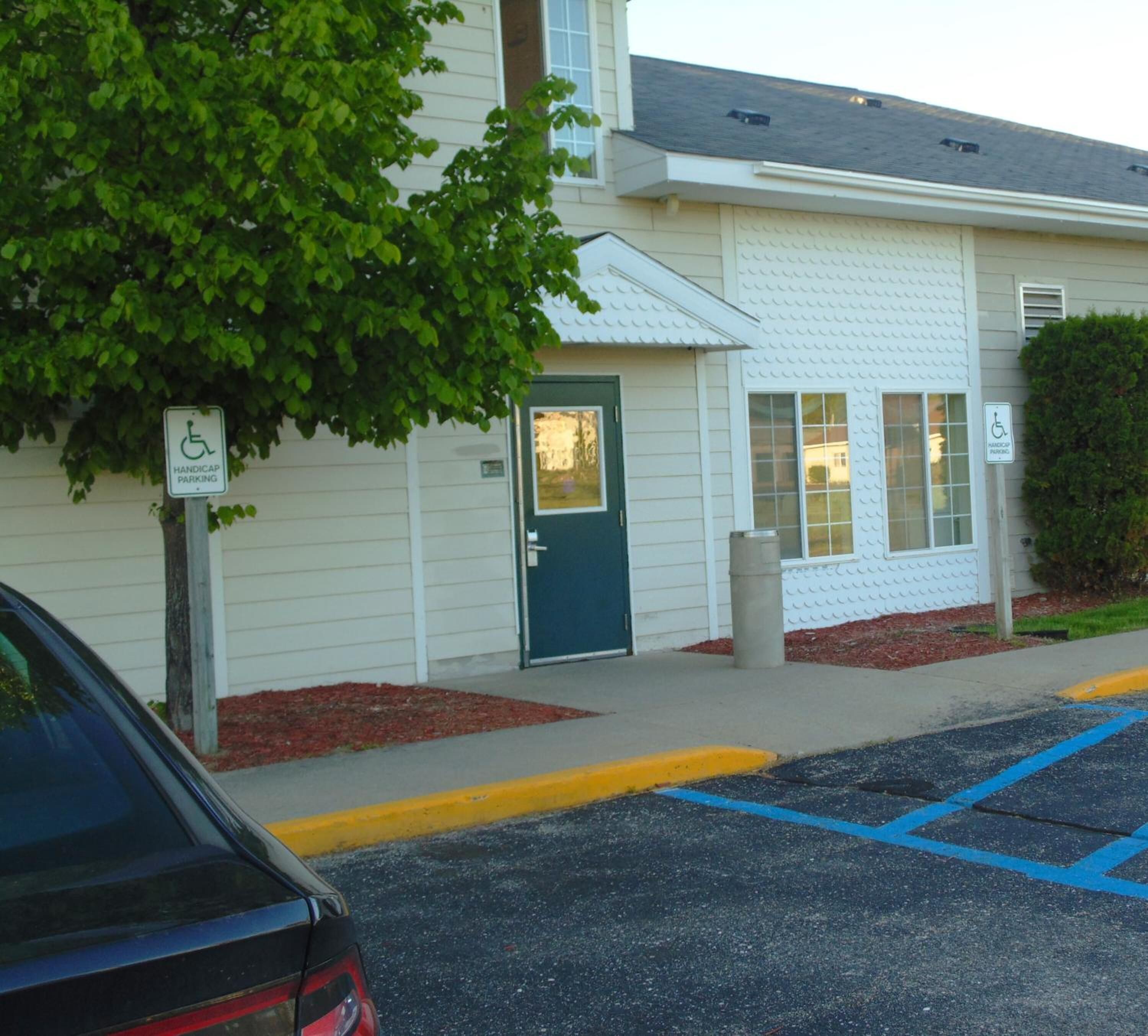 A building with handicap parking signs, a blue door, and a parking lot with blue handicapped parking spaces.