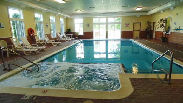 An indoor swimming pool with lounge chairs and a hot tub area. - American Inn and Suites Houghton Lake (Houghton Lake)