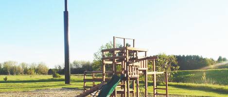 Ein Spielplatz mit Rutsche und Klettergerüsten, umgeben von einer Wiese.