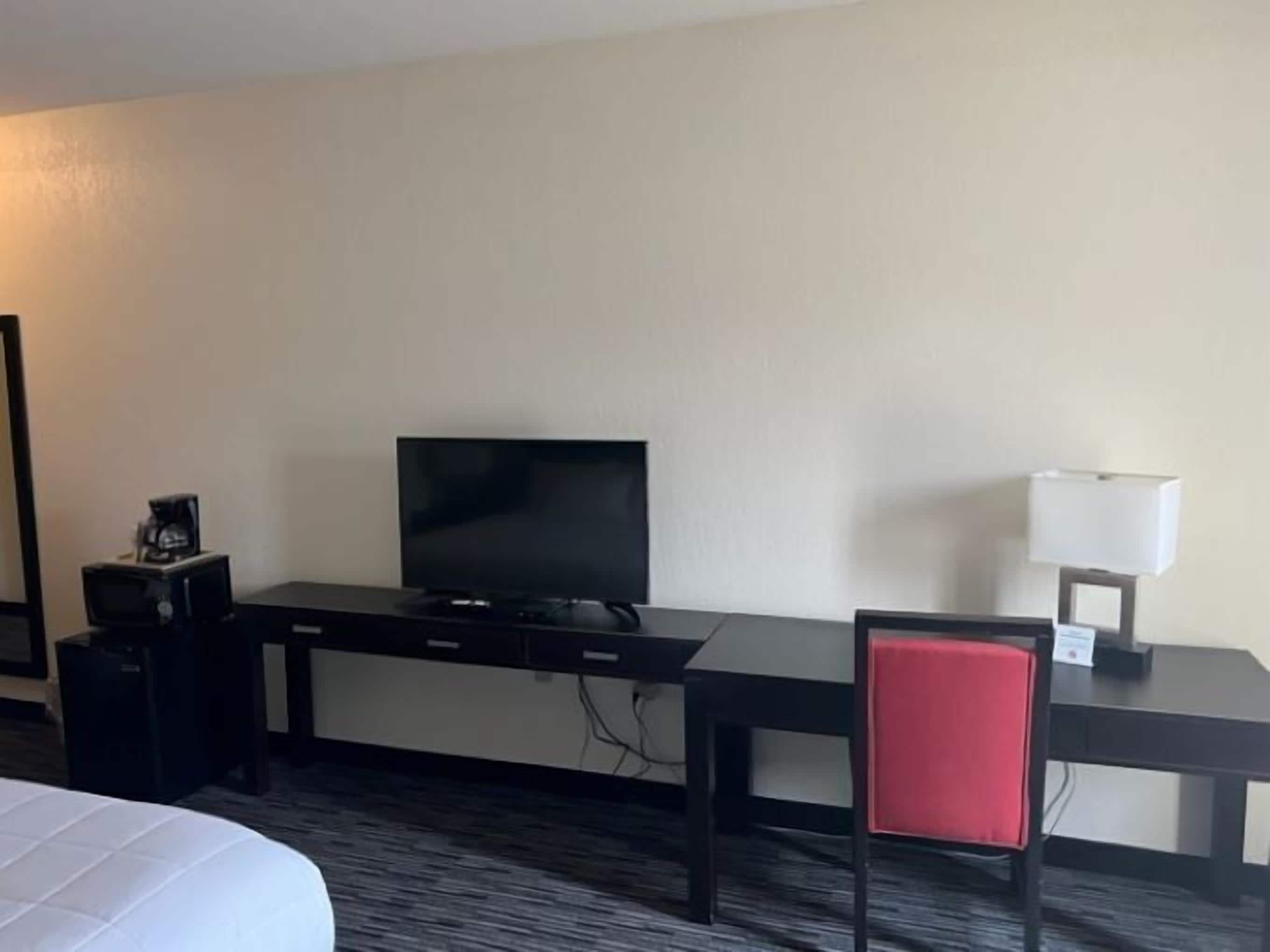 Habitación de hotel con cama, escritorio con televisor, cafetera y una silla roja.