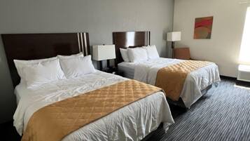 Quarto de hotel com duas camas, cada uma com cabeceira, roupa de cama branca e manta acolchoada marrom. Há abajures e uma pintura na parede.