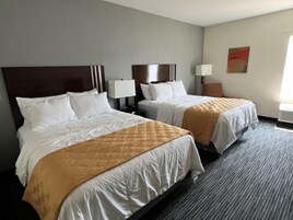 Quarto de hotel com duas camas, cada uma com cabeceira, roupa de cama branca e manta acolchoada marrom. Há abajures e uma pintura na parede.