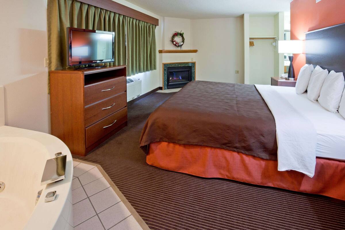 Una habitación de hotel con cama, televisión, chimenea, cómoda de madera y baño.