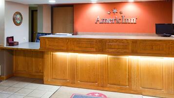A reception desk with a wooden finish, a clock on the wall, and a carpet with the American Inn logo.