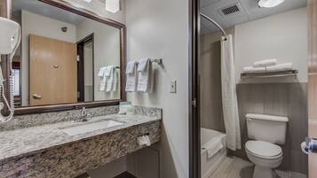 Un baño moderno con encimera de granito, un espejo, inodoro y cabina de ducha.